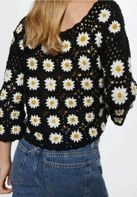 Gehaakt topje in zwart met een bloemmotief met grote witte madeliefjes met gele kernen. Heeft driekwart mouwen en een open geweven ontwerp.