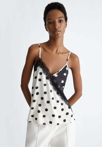 Camisola di satin con un motivo a pois bianco e nero, caratterizzata da un bordo in pizzo lungo il collo e un design asimmetrico del colore.