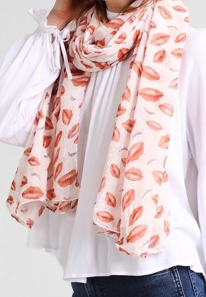 Lyserød tørklæde med røde læbestifttryk og små lukkede øjenvippe-mønstre, båret over en hvid bluse og blå jeans.