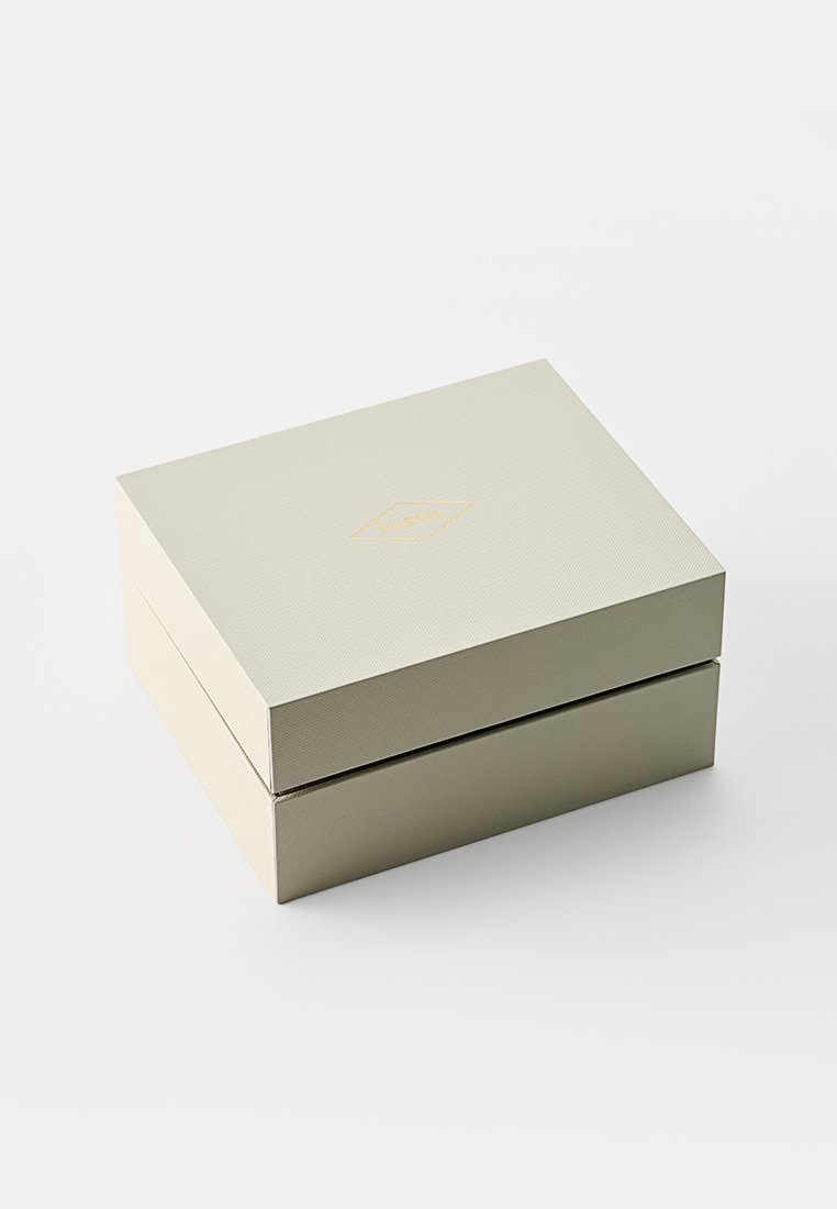 Boîte carrée de couleur beige clair avec un extérieur texturé et un logo doré en relief sur le dessus, présentant un design à plusieurs niveaux avec un compartiment caché.