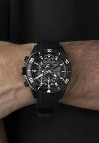 Montre en quartz noire avec un boîtier rond, un bracelet en caoutchouc et des marquages blancs ; elle présente des touches rouges et plusieurs cadrans pour la mesure du temps.