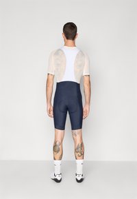 Ropa de ciclismo con un pantalón ajustado azul marino y una parte superior de malla blanca. El diseño notable incluye piernas tatuadas y un área de asiento acolchada para mayor comodidad.