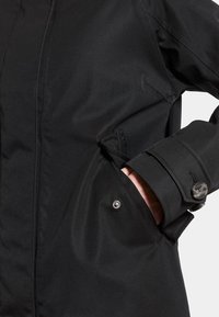 Zwarte waterdichte jas met een gladde textuur, voorzien van een ritsluiting, zijzakken en knoopmanchetten voor een verstelbare pasvorm.