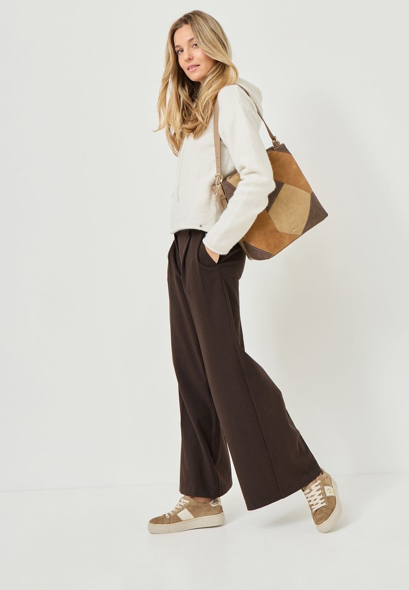 Ljusgrå hoodie, bruna veckade byxor med vida ben och beige sneakers, kombinerat med en geometrisk beige och brun toteväska.