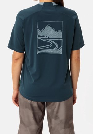 Person wearing a dark blue short-sleeve shirt with a stylized mountain and road graphic on the back, paired with gray shorts.