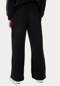 Pantalones de chándal negros de pierna ancha, fabricados con un tejido suave, que cuentan con un corte holgado, cintura elástica y sin patrones o detalles de hardware visibles.