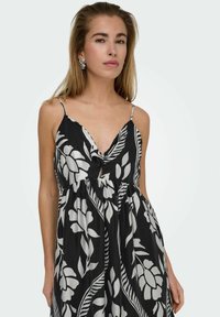 Zwart-wit bloemenpatroond jurk met een V-hals, dunne bandjes, gather taille en losse pasvorm. Doorzichtige textuur en gedurfde grafische ontwerpen.