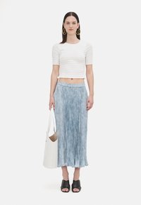 Hvit, ribbet kortermet topp kombinert med en lys blå, plissert maxiskjørt. Modellen holder en hvit tote bag og har på seg svarte, åpne sko.