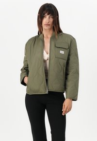 Giacca bomber imbottita verde oliva con zip frontale, polsini a coste e taschino con logo sul petto. Tessuto in poliestere liscio.