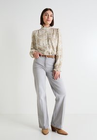 Blusa de patrón beis fluida con muñecas recogidas, combinada con jeans de pierna ancha grises claros y botas de tobillo de tacón marrones.