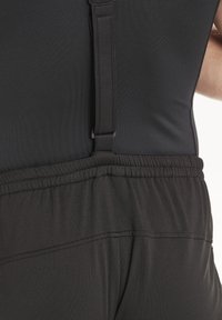 Tenue de sport noire avec des bretelles réglables et une taille élastique. Texture de tissu lisse et détails de couture soignés.