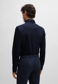 Marineblaues Langarmhemd mit strukturiertem Kragen und Knopfmanschetten, kombiniert mit marineblauen, strukturierten Hosen mit elastischem Bund und Seitentaschen.