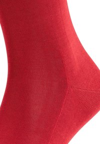 Rød bomuldsstrømpe med en glat tekstur og ribbet design, der har forstærkede syninger ved hælen og tåen for øget holdbarhed.