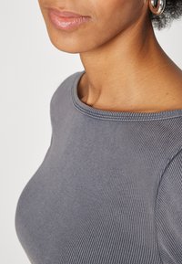 Grå ribbad topp med rund halsringning och korta ärmar, tillverkad av mjukt tyg med synliga sömnadsdetaljer.