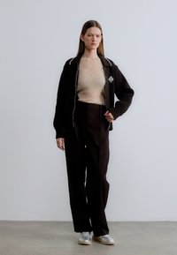 Veste noire côtelée à fermeture éclair avec bordure blanche, haut côtelé beige, pantalon noir ample et baskets grises. Design simple avec des couleurs neutres.