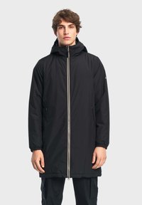 Cappotto lungo nero con cappuccio, dotato di zip frontale completa, polsini elasticizzati e due tasche laterali. Texture liscia e design leggero.