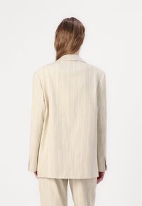 Beige gestreepte blazer van lichtgewicht stof, met een klassieke snit, gekartelde revers en een ventileerde achterkant. Gecombineerd met bijpassende broek.
