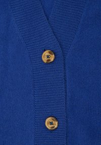 Blauwe gebreide cardigan met een V-hals ontwerp. Beschikt over twee ronde, gemarmerde knopen en een ribbelstructuur langs de randen. Zacht materiaal.