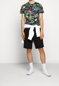 Tričko s barevným tropickým potiskem; černé šortky; bílý svetr uvázaný v pase; bílé tenisky; ponožky ke kotníkům.