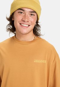 Sennepsgul kortærmet t-shirt med blød tekstur og Quiksilver-logo trykt i lys gul på venstre side. Buet halsudskæring.