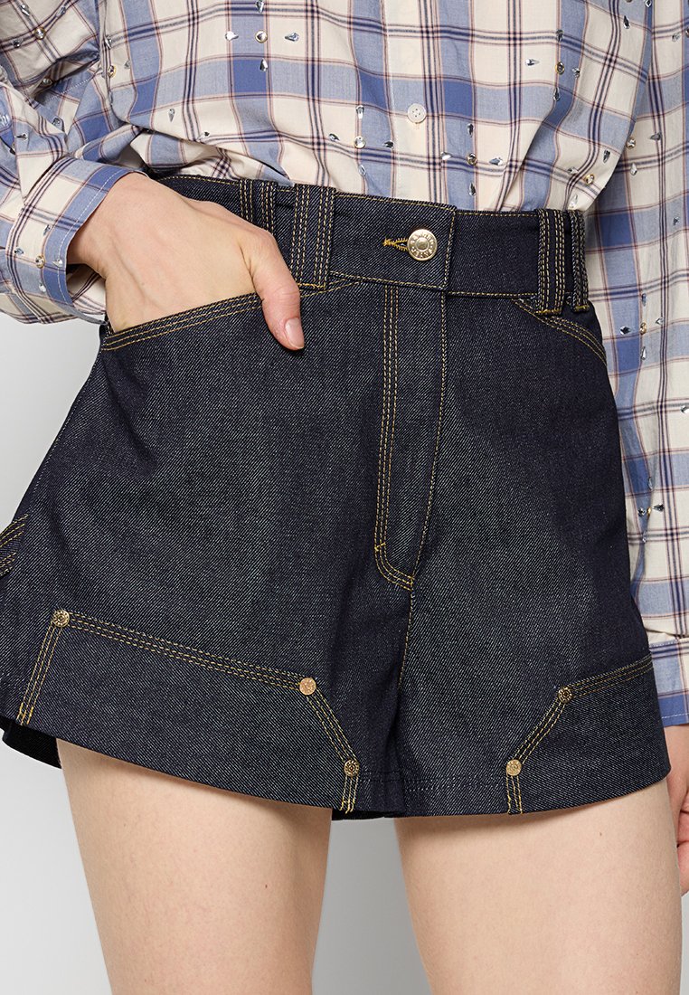 Shorts de mezclilla oscura con costuras amarillas, de tiro alto y múltiples bolsillos. Textura suave con un diseño estructurado.