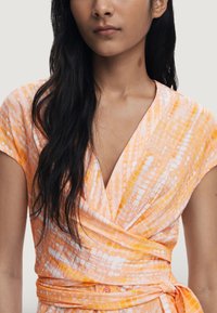 Vestido envolvente en naranja y blanco, con rayas diagonales, mangas cortas y un lazo en la cintura. Textura suave y diseño de escote en V.