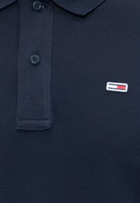 Navy blue polo shirt with two buttons and a small rectangular logo patch with red, white, and blue on the left chest.