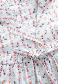 Pijamale în dungi albastre deschise cu trandafiri roșii și ilustrații mici cu câini, având o cămașă cu nasturi și pantaloni cu talie elastică legați cu o fundă.