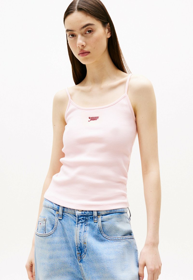 Hellsrose-farbenes, enges Trägershirt mit dünnen Trägern, das ein kleines rotes "Tommy Jeans"-Logo auf der Brust zeigt, kombiniert mit hellblauen Denim-Jeans.
