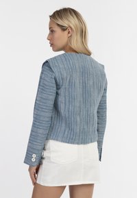 Blauwe gestreepte cropped jasje van textuurstof met drie-knopen manchetten, gecombineerd met een witte denim rok.