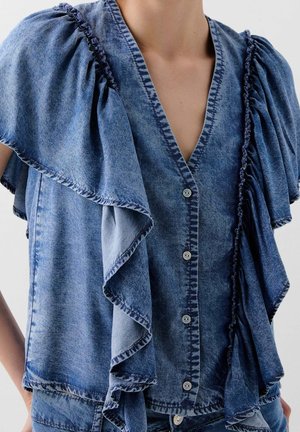 Denim blouse with large ruffled sleeves, button-down front, and faded blue stonewash texture worn by a person with visible neck and upper torso.