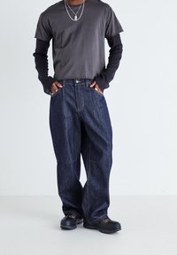 Dark blue denim jeans with a loose fit, completed with a gray t-shirt layered over a black long-sleeve shirt, and black shoes.