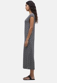 Vestido holgado de largo hasta la rodilla en un patrón geométrico en blanco y negro, con mangas cortas tipo capucha y laterales con aberturas. Llevado con sandalias planas negras.