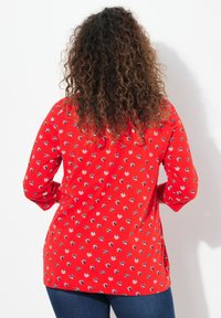 Rotes Langarmoberteil mit kleinen floralen Mustern in Weiß und Blau. Weicher Stoff mit lockerer Passform und runder Saum, kombiniert mit dunkler Denim.