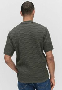 Korte mouwen poloshirt in donkergroen, gestructureerde stof met een subtiel patroon, ribgebreide kraag en rechte zoom. Zicht van achteren.