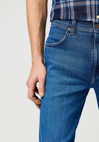 Jeans de mezclilla azul con un corte slim, que presentan un diseño clásico de cinco bolsillos, un suave efecto de desgaste y terminados con herrajes en tono cobre.