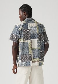 Košulja kratkih rukava s patchwork dizajnom u plavim, zelenim i smešnim tonovima; sadrži cvjetne i geometrijske uzorke. Prikazan je stražnji pogled.