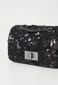 Borsa a tracolla nera in paillettes con superficie testurizzata, tracolla a catena, forma rettangolare e dettaglio di chiusura a scatto in argento.