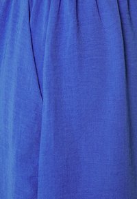 Tejido azul brillante con textura visible y sutiles pliegues, que destacan los patrones tejidos y la caída suave.