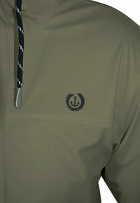 Olivgrüne wasserdichte Jacke mit einem Reißverschluss in der Vorderseite, verstellbarem marineblauen Kordelzug und einem Anker-Logo auf der Brust. Glatte Oberfläche.