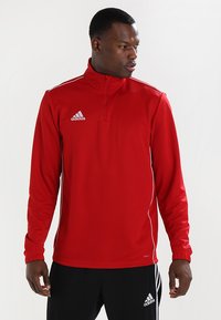 Rød atletisk genser med kvart-zip-kra, lange ermer og hvite detaljer. Har Adidas-logoen på brystet. Glatt polyester materiale.