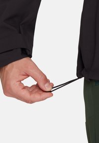 Black jacket with adjustable elastic cuffs, showing a hand pulling the cord. Smooth texture with minimal seams and an outdoor design.