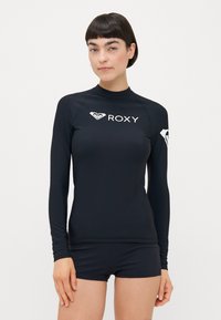 Crni rash guard dugih rukava izrađen od rastezljivog materijala s visokom ovratnikom, s bijelim logotipom "ROXY" i božnim emblemom.