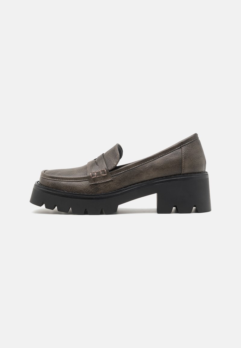 Brown leather loafers with a decorative strap, chunky black rubber sole, and textured upper. Features a slight heel and a smooth finish.
