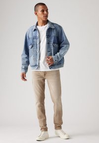 Camisola de ganga em azul claro com fecho de botão, apresentando dois bolsos no peito. Combinada com calças ajustadas em bege e ténis brancos.