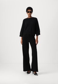 Μαύρο oversized πουλόβερ με φαρδιά μανίκια, συνδυασμένο με μαύρα ψηλόμεσα παντελόνια σε ίσια γραμμή και μαύρες ψηλές γόβες. Μοντέρνα, κομψή εμφάνιση.