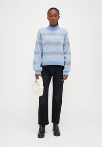 Pull en tricot bleu clair avec un motif rayé, col rond et poignets côtelés, associé à un jean noir à jambe droite et des bottes noires chunky.