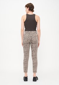 Hnědý tílko, béžové kalhoty s leopardím potiskem, úzký střih, hladká textura, délka po kotníky, v kombinaci s černými botami.