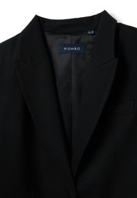 Blazer nero con risvolti a lancia, tasca singola sul petto e cuciture dettagliate. Etichetta interna con scritto "PIOMBO". Tessuto liscio, design sartoriale.