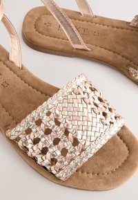 Platte sandalen met een geweven metallic band in tinten rozenhout en lichtgoud, met een bruine suède voetbed en eenvoudige beige bandjes.